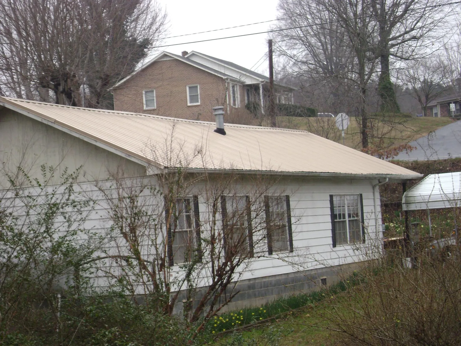 Tan metal roof on a white sided house set into a hillside — Commercial Roofing by Roofing Brothers in Ryde